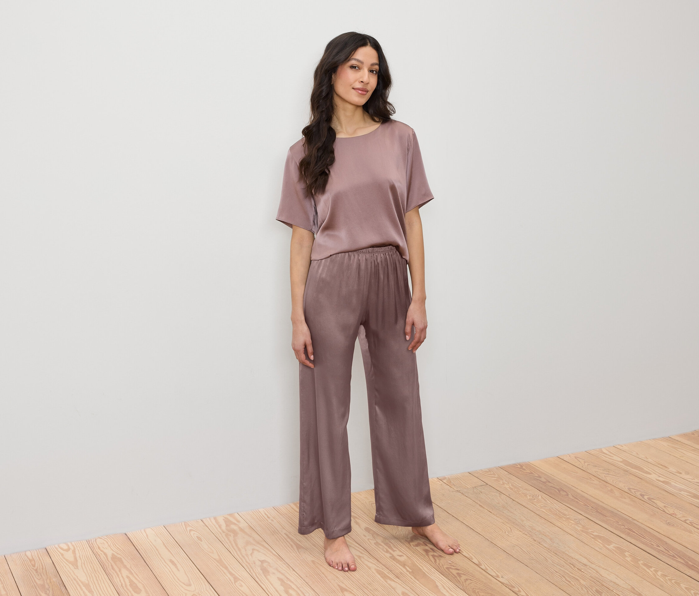 Žena pózuje v saténovém pyžamu skládajícím se z trička a kalhot.