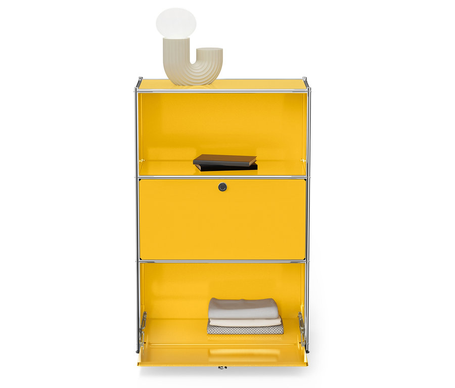 Žlutá skříňka se stříbrným rámem, nahoře lampa a kniha, dole složené ručníky.