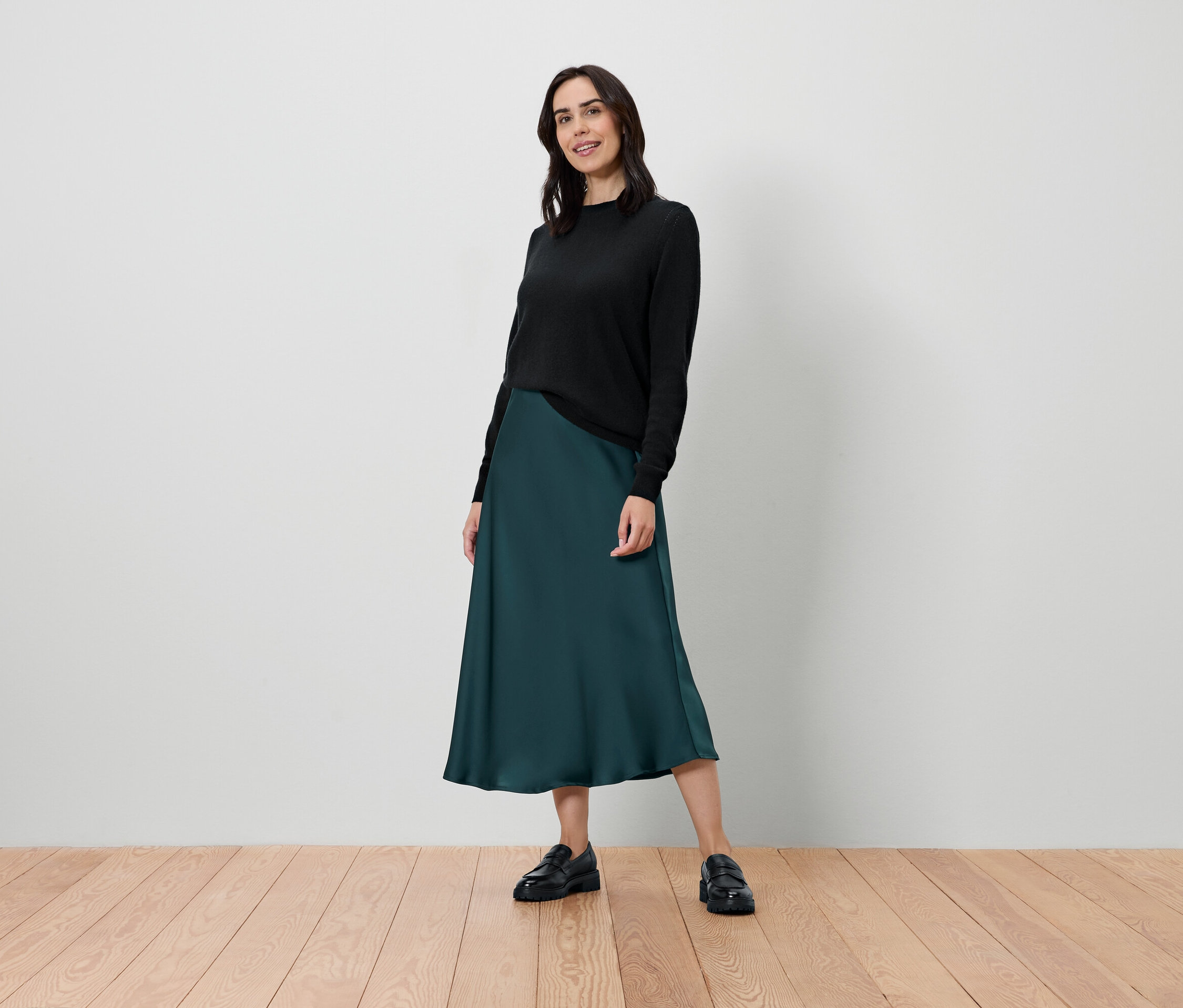 Žena stojí a pózuje v černém svetru a tmavě zelené sukni.