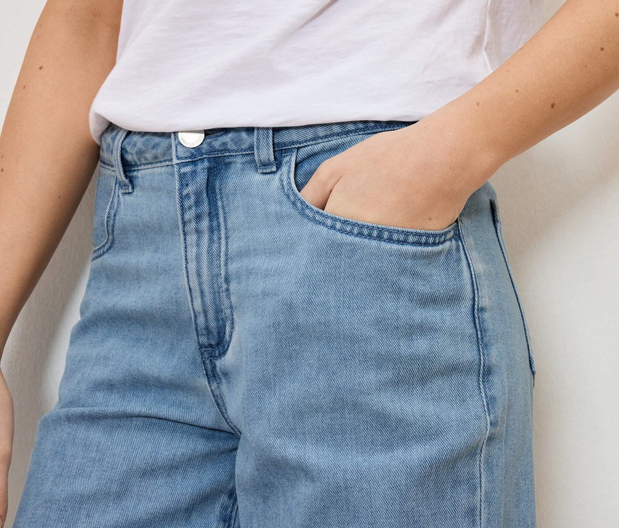 Detailní záběr ženy ve světle modrých džínách a bílém tričku, která má ruku v kapse.