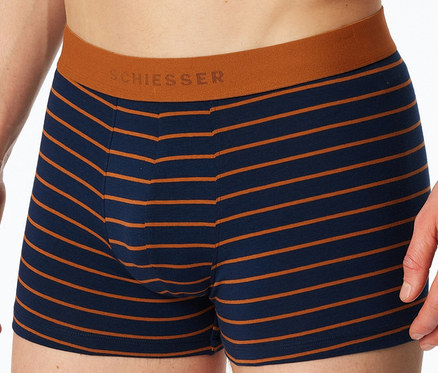 Detail osoby v tmavě modrých a oranžových proužkovaných boxerkách SCHIESSER s oranžovým pasem.