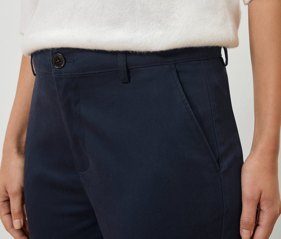 Detailní záběr osoby v tmavě modrých kalhotách a bílém svetru.