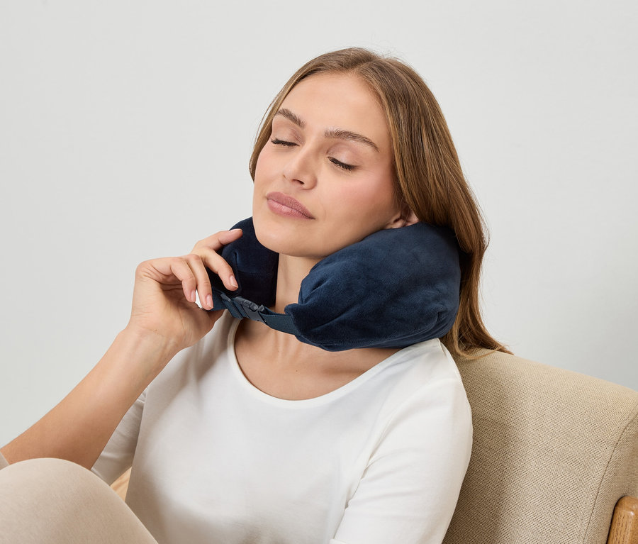 Žena se zavřenýma očima nosí tmavě modrrou opěrku krku, zatímco sedí v křesle.