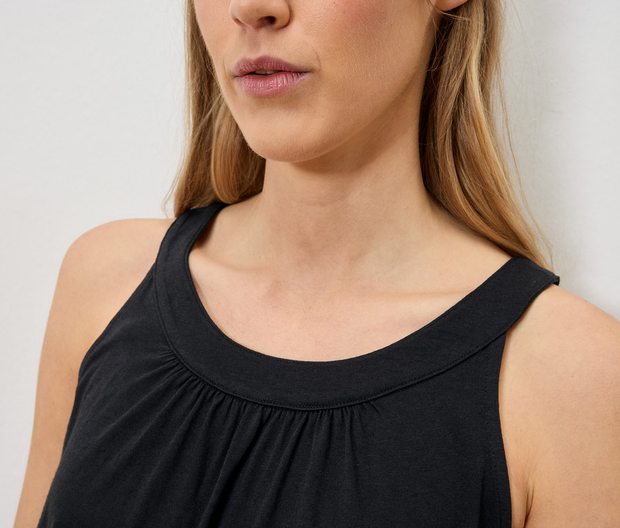 Detailní záběr ženy s blond vlasy v černém tílku bez rukávů.