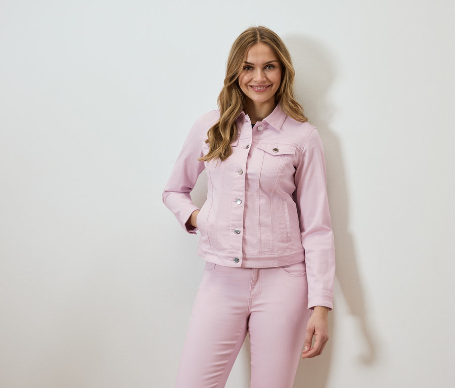 Žena má na sobě růžovou džínovou bundu a odpovídající džíny.