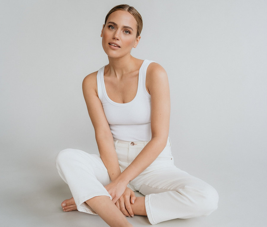 Žena sedí bosá se zkříženýma nohama na zemi, oblečená v bílém tílku a bílých džínách Angels »Evy Cool« O-shape.