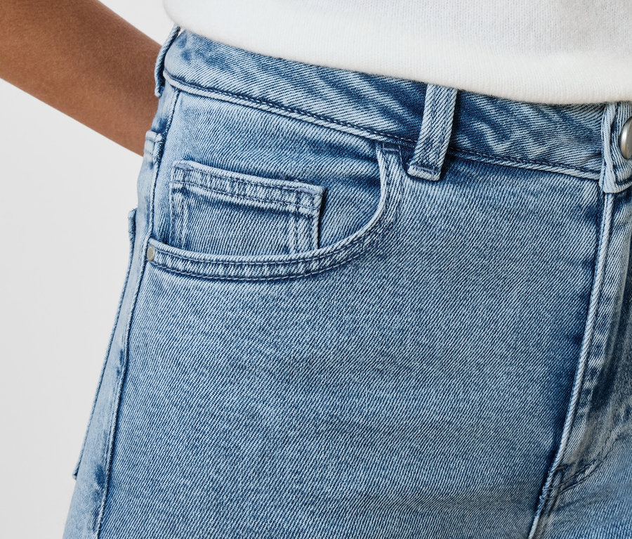 Detailní záběr na světle modré džínové kalhoty s kapsami a knoflíkem.