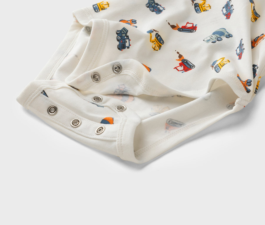 Detailní záběr na bílé dětské body s potiskem stavebních vozidel a patentkami.