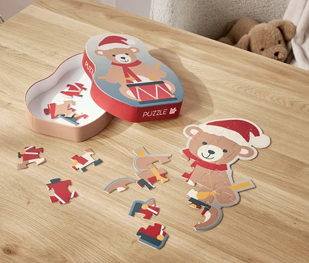 Na stole leží rozložené puzzle s motivem medvídka v santovské čepici a jeho krabička.