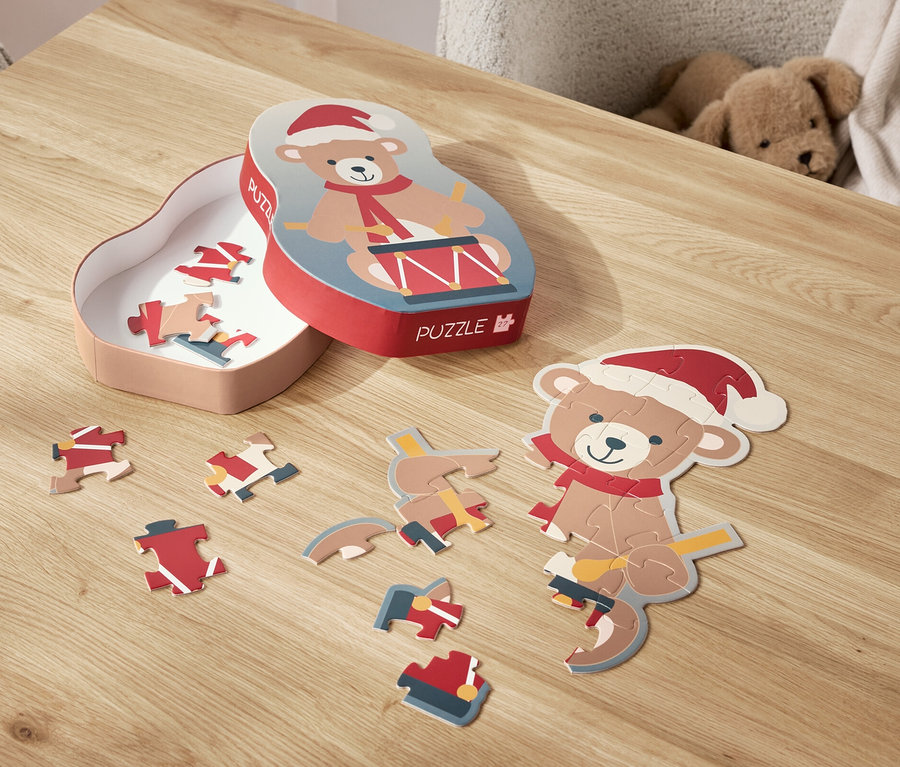 Na stole leží rozložené puzzle s motivem medvídka v santovské čepici a jeho krabička.