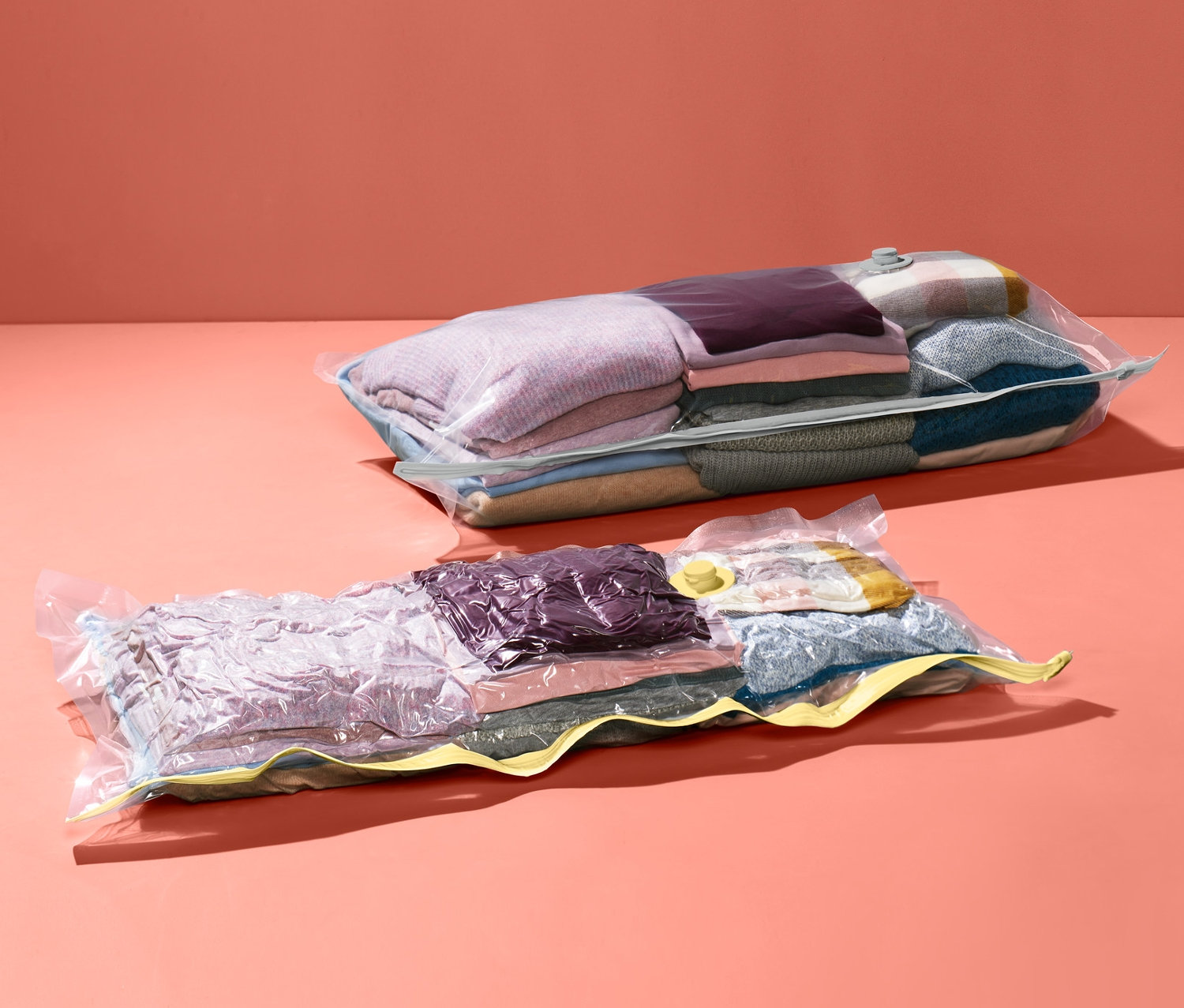 Dva vakuové úložné pytle s oblečením na korálovém pozadí.