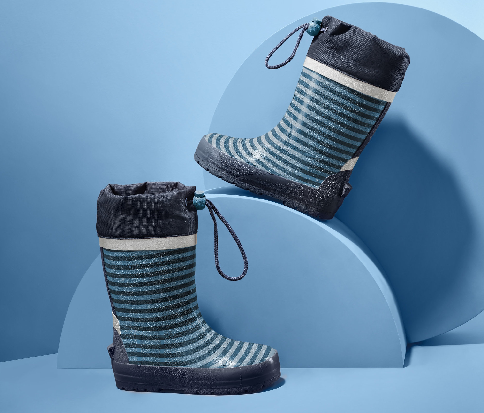 Dvoje dětské proužkované holínky do deště na modrém pozadí.