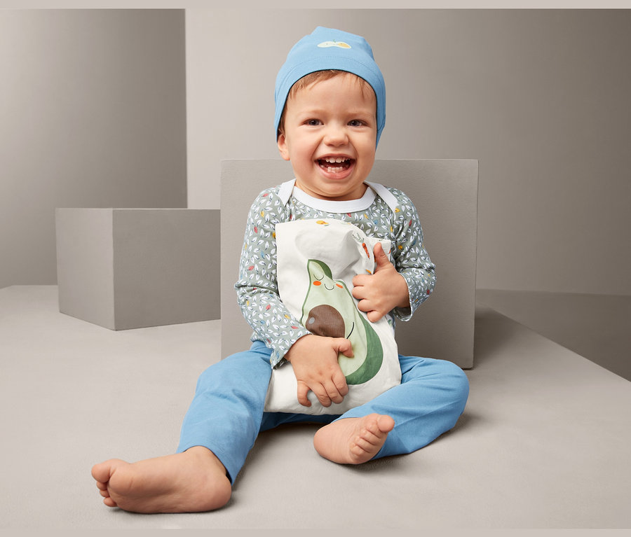 Usmívající se dítě sedí a drží hřejivý polštářek s výplní z řepkových semen s potiskem avokáda.