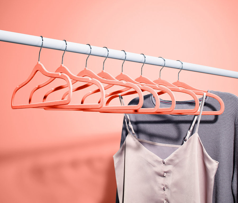 Na bílé tyči visí osm ramínek na šaty. Na jednom z nich visí šedý svetr a tílko.