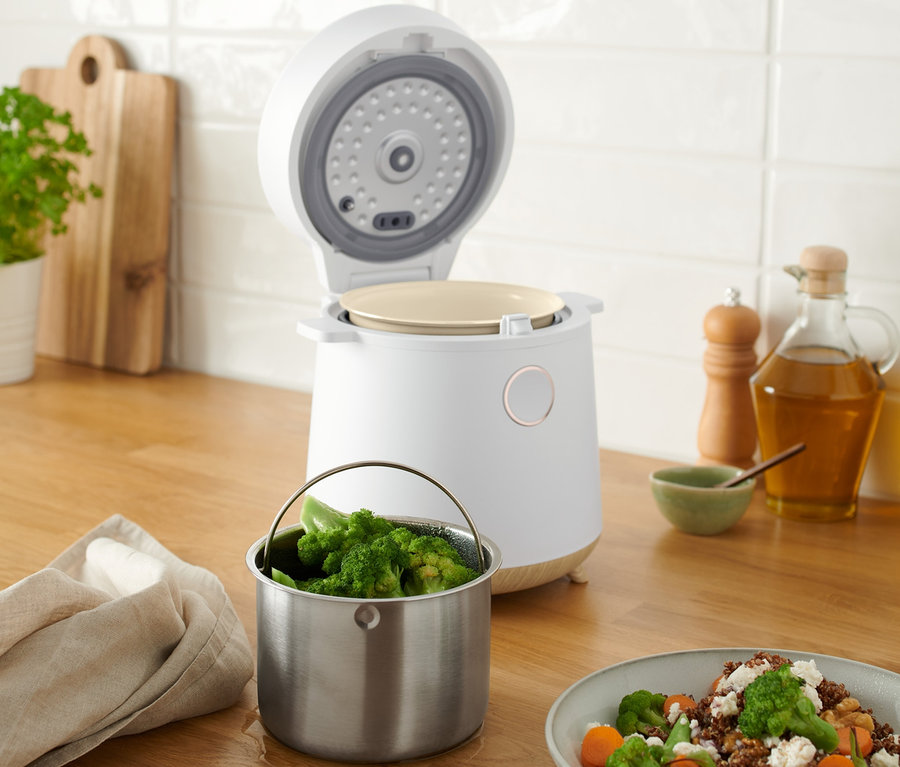 Na dřevěné desce stojí otevřený multifunkční vařič, vedle něj je miska s brokolicí a mrkví.