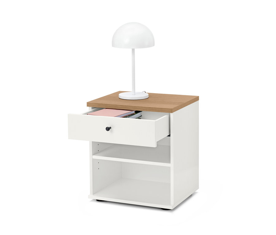 Bílý noční stolek »Bekeson« s hnědou deskou a otevřenou zásuvkou. Na stolku stojí bílá lampa.