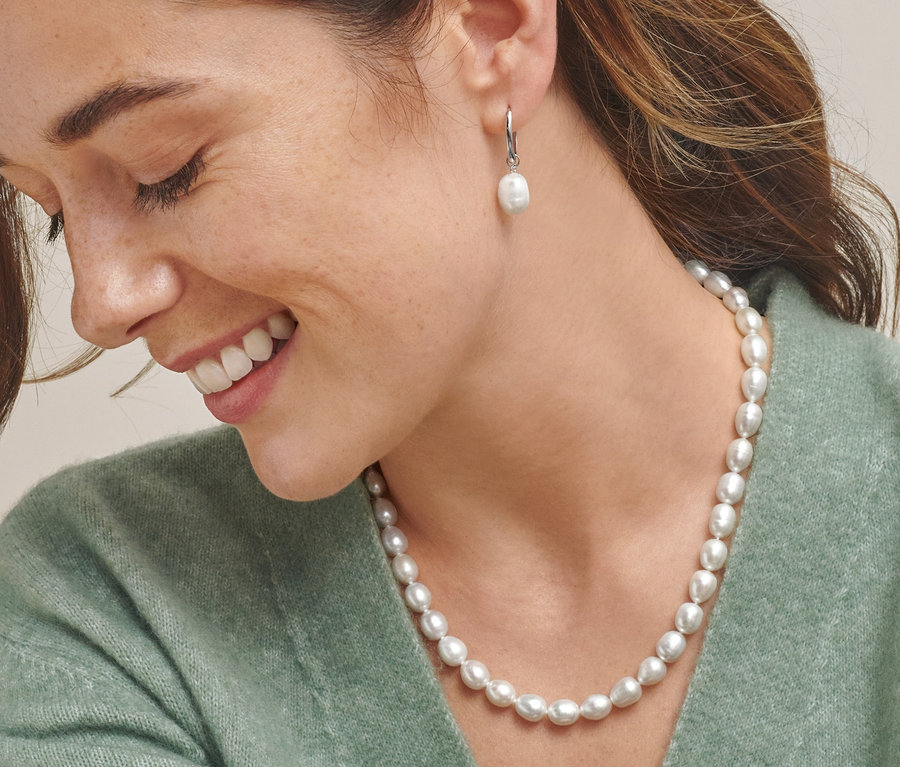 Žena nosí kreolky z rhodiovaného stříbra a náhrdelník z uměle pěstovaných sladkovodních perel.