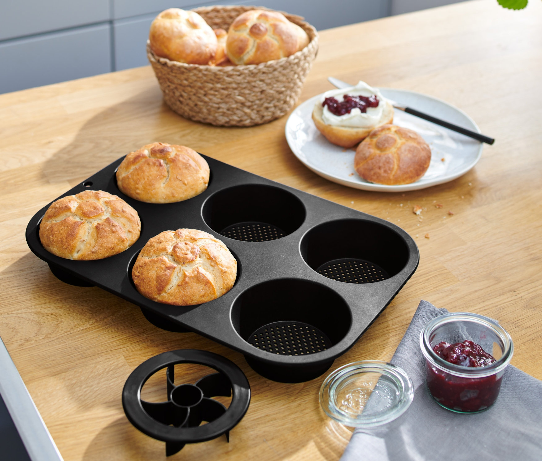 Čtyři housky v černé perforované formě na pečení housek na dřevěném stole.