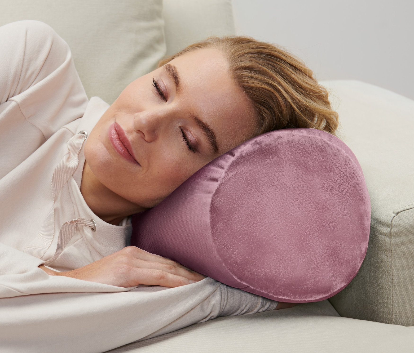 Žena spí na béžové pohovce s relaxačním polštářkem.