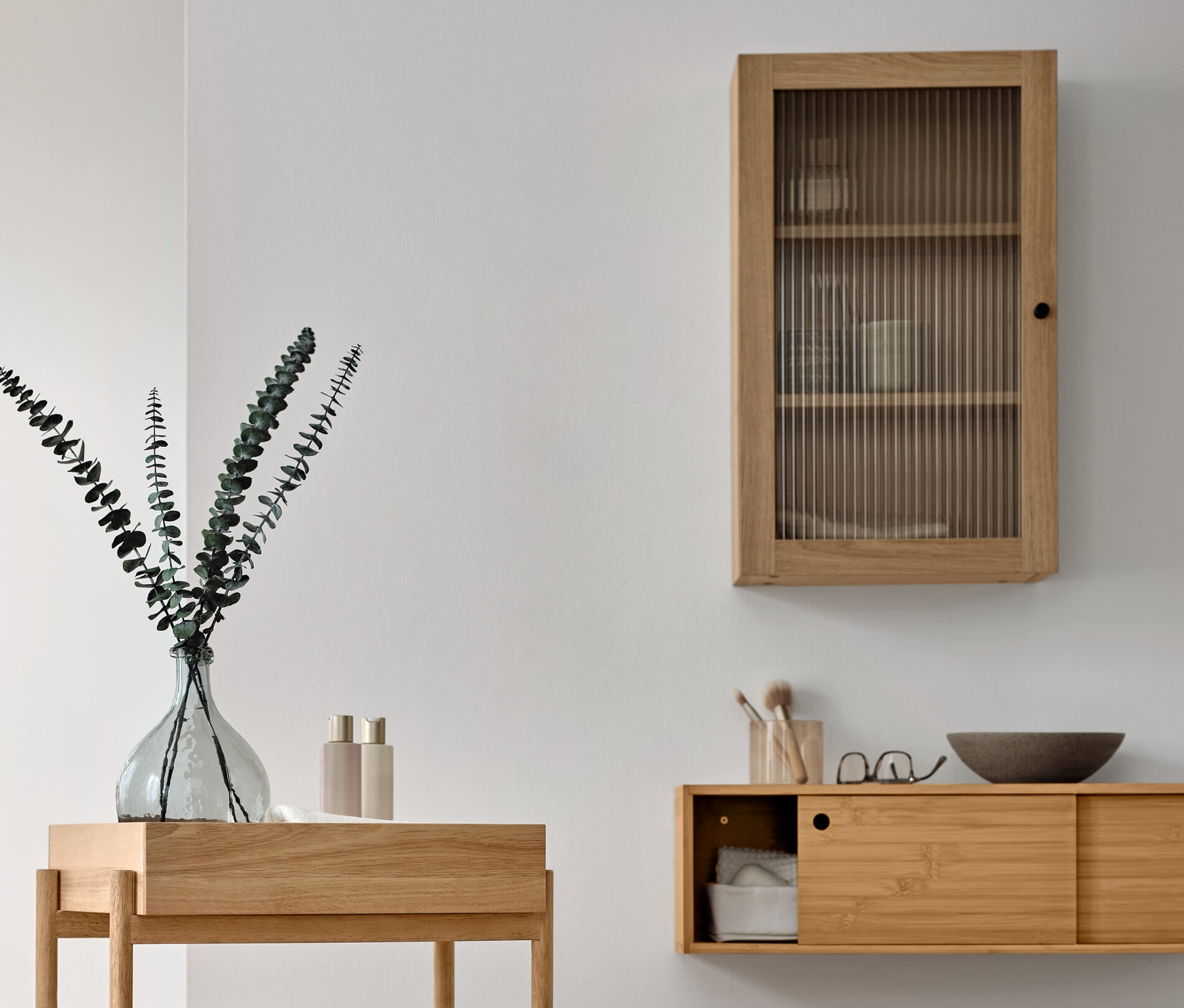 Interiér koupelny s dřevěným stojacím regálem se 3 přihrádkami, nástěnnou skříňkou s dvířky s rýhovaným sklem a věšákem na ručníky z masivního dřeva.