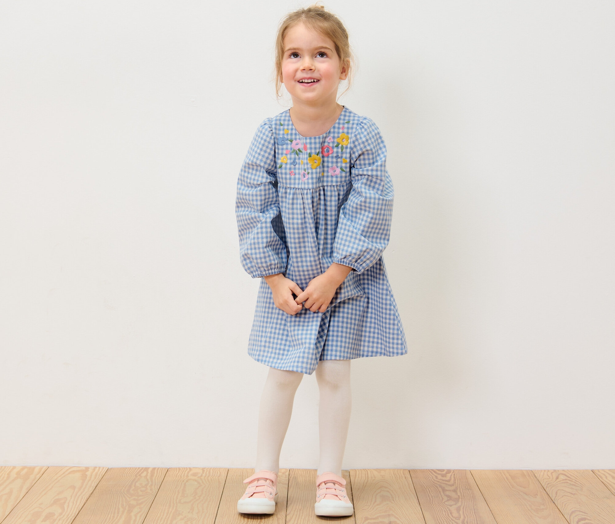 Usmívající se dívka má na sobě tkané šaty s květinovou výšivkou.