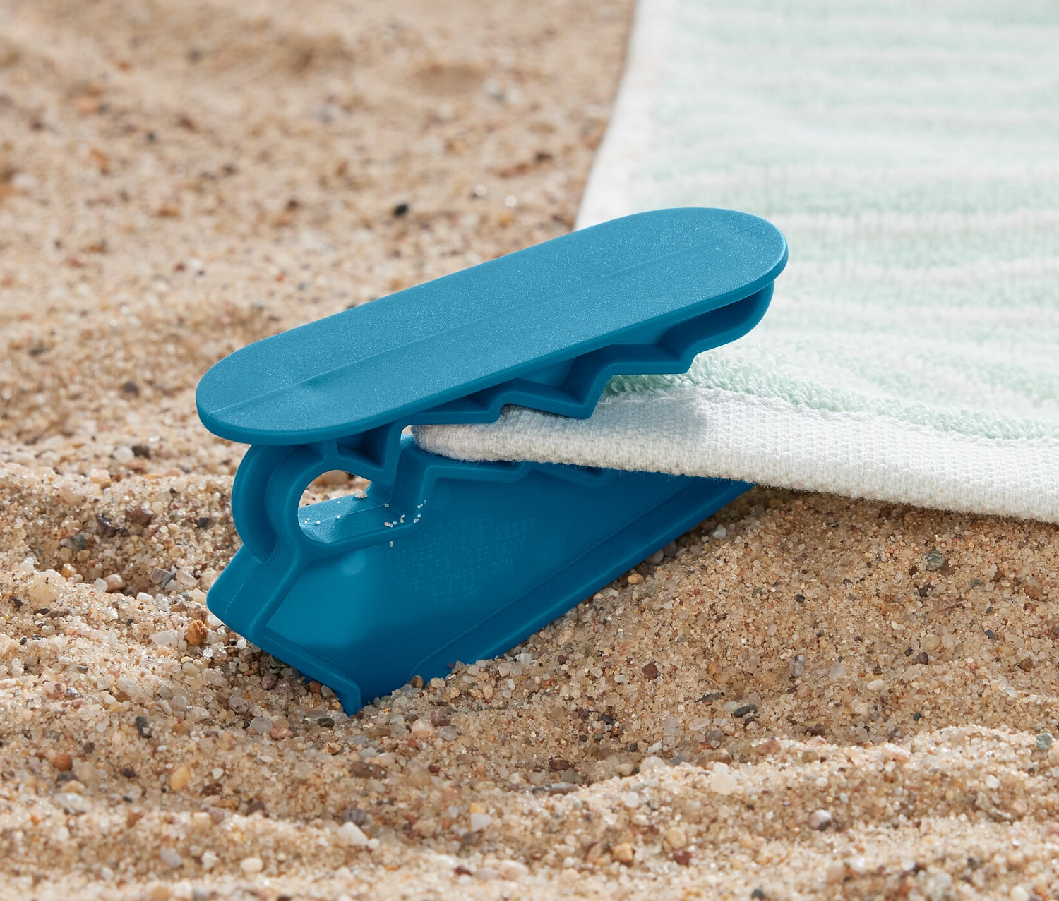 Modrá svorka na ručníky, 4 ks, připevněná k ručníku na písku.