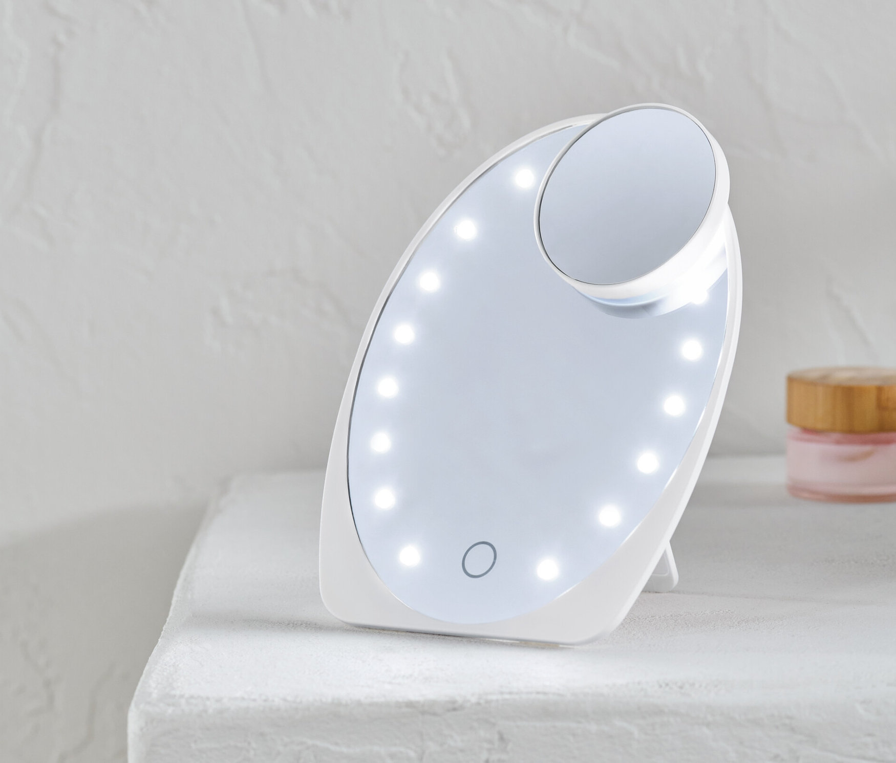 Bílé kosmetické zrcátko s LED osvětlením stojí na bílém povrchu.