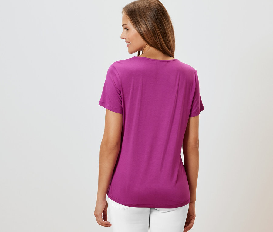 Žena zezadu v tričku s detailem skladů, bobulová a bílých kalhotách.