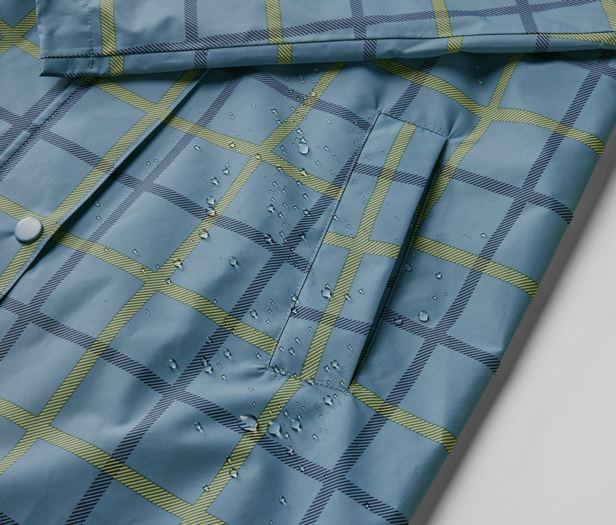 Detail modré bundy do deště s kostkovaným vzorem a kapkami vody.