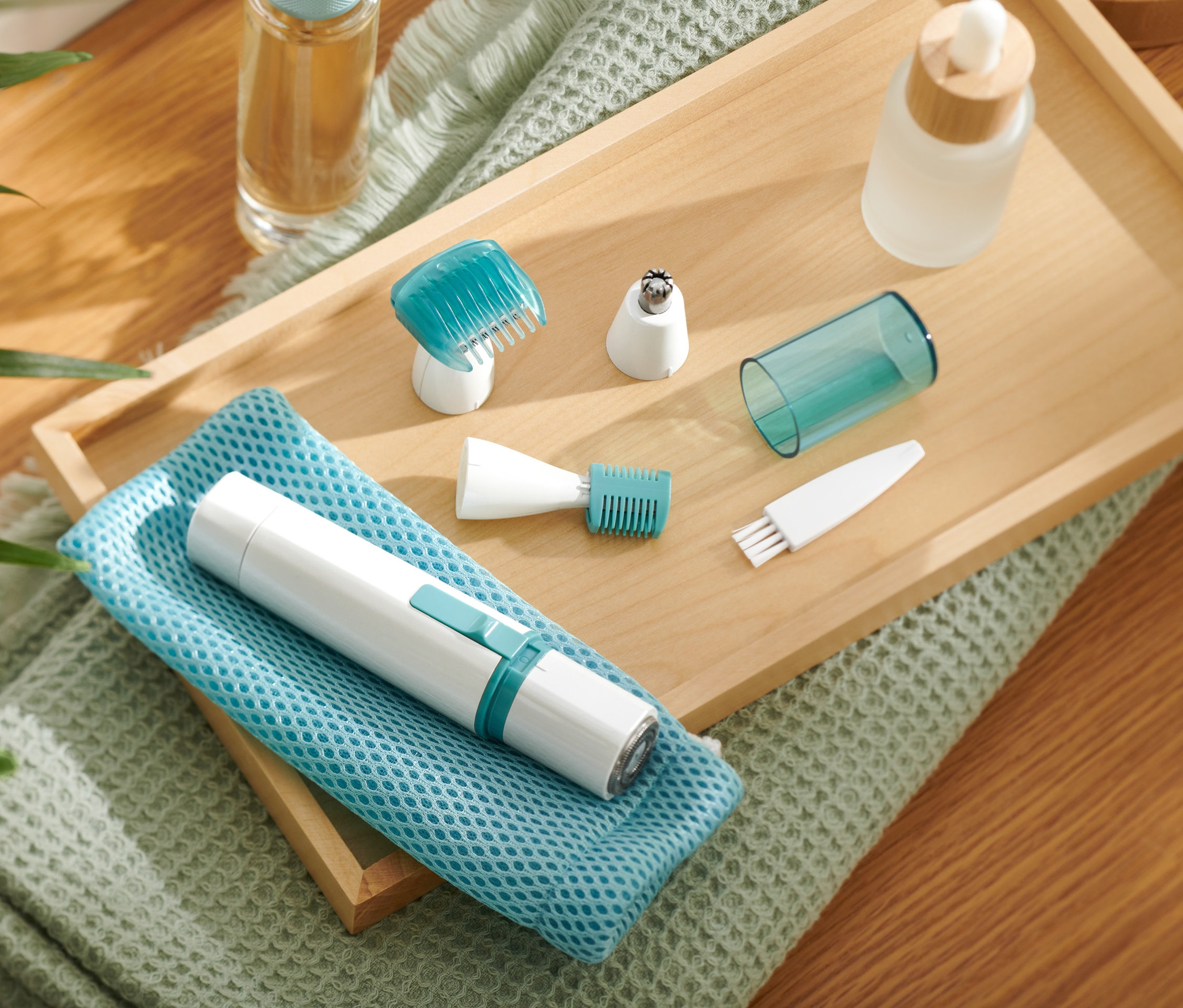 Elektrický zastřihovač chloupků na tělo a obličej s nástavci na dřevěném podnosu.