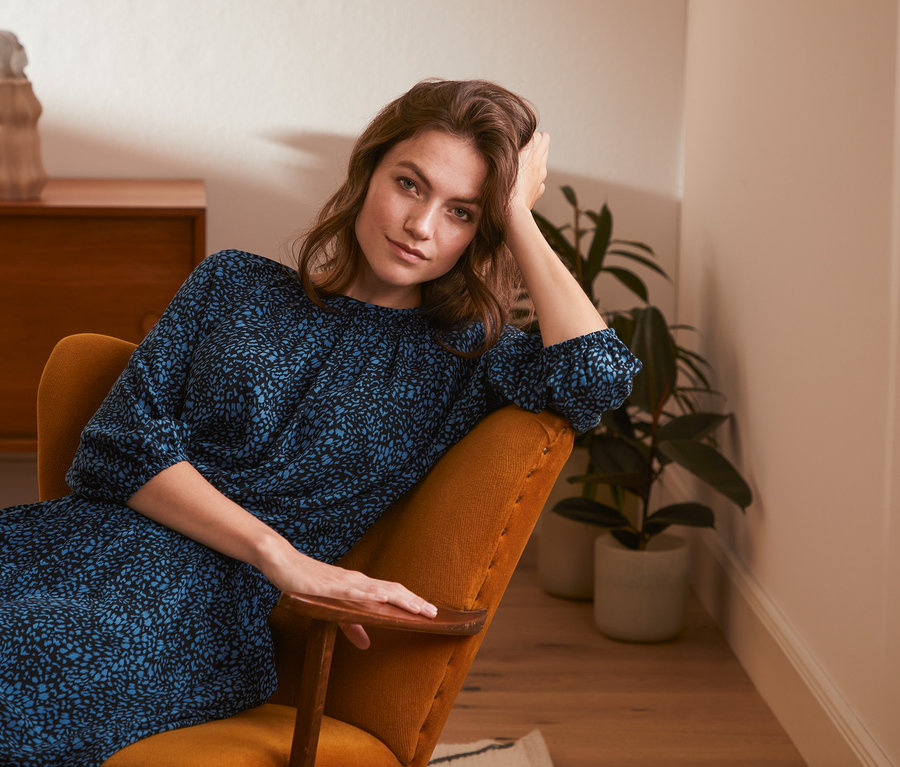 Žena sedí v křesle a má na sobě halenku s potiskem.