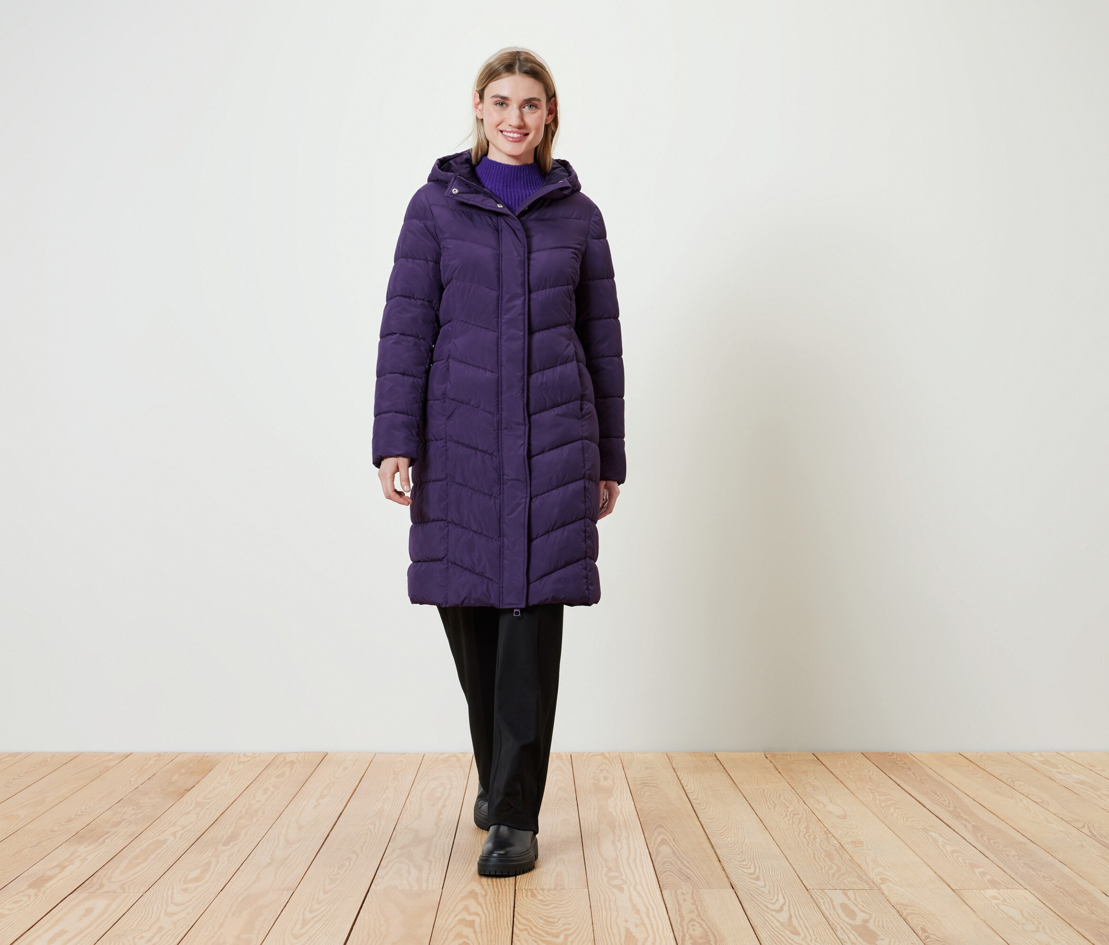 Žena v dlouhé fialové prošívané bundě s kapucí.