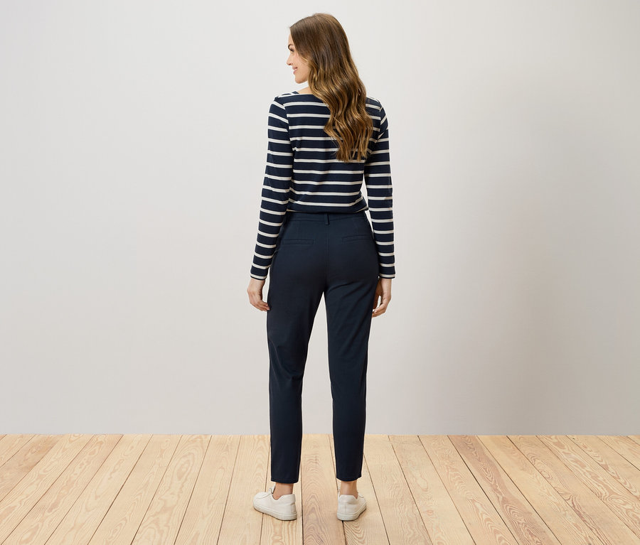 Zezadu vidíme ženu s hnědými vlasy v tmavě modrých kalhotách a pruhovaném tričku.