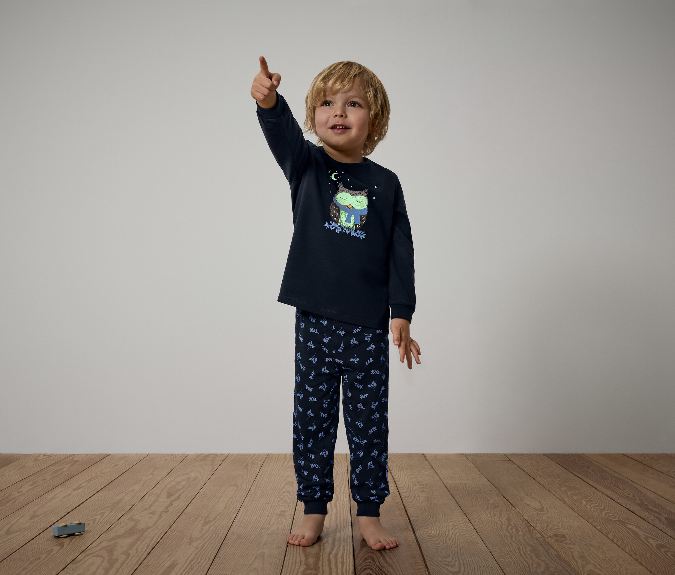 Chlapec v tmavě modrém pyžamu s potiskem sovy ukazuje prstem nahoru.