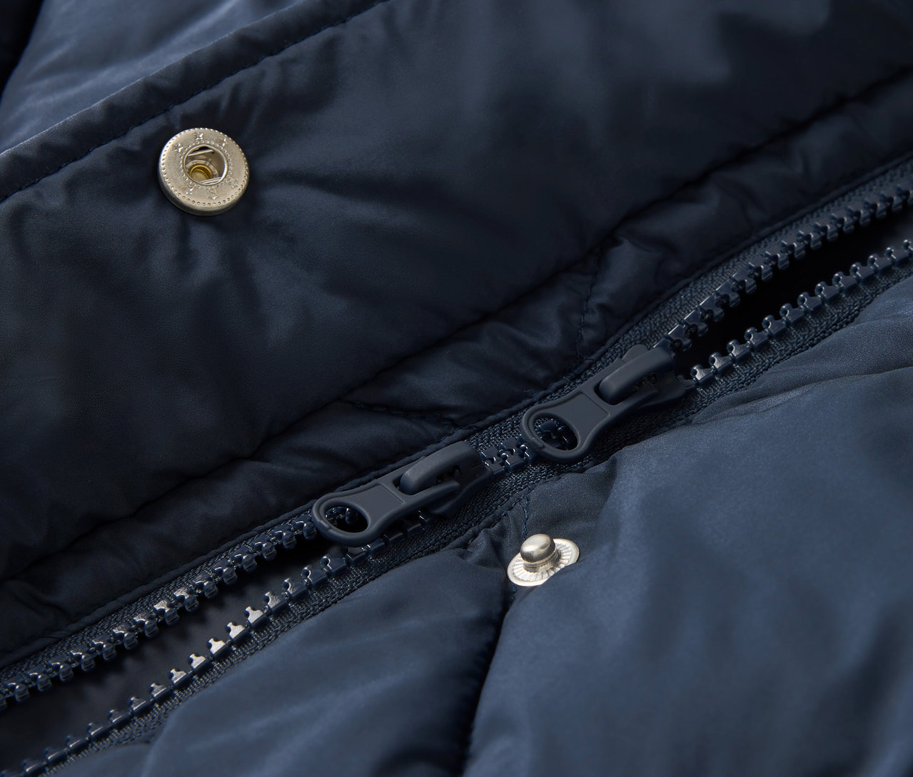 Detail modré prošívané bundy se zipem a patentkami.