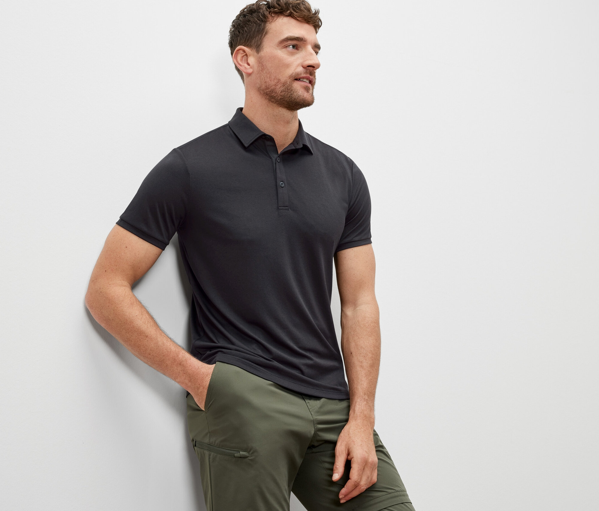 Muž opřený o zeď má na sobě antracitovou funkční polokošili.