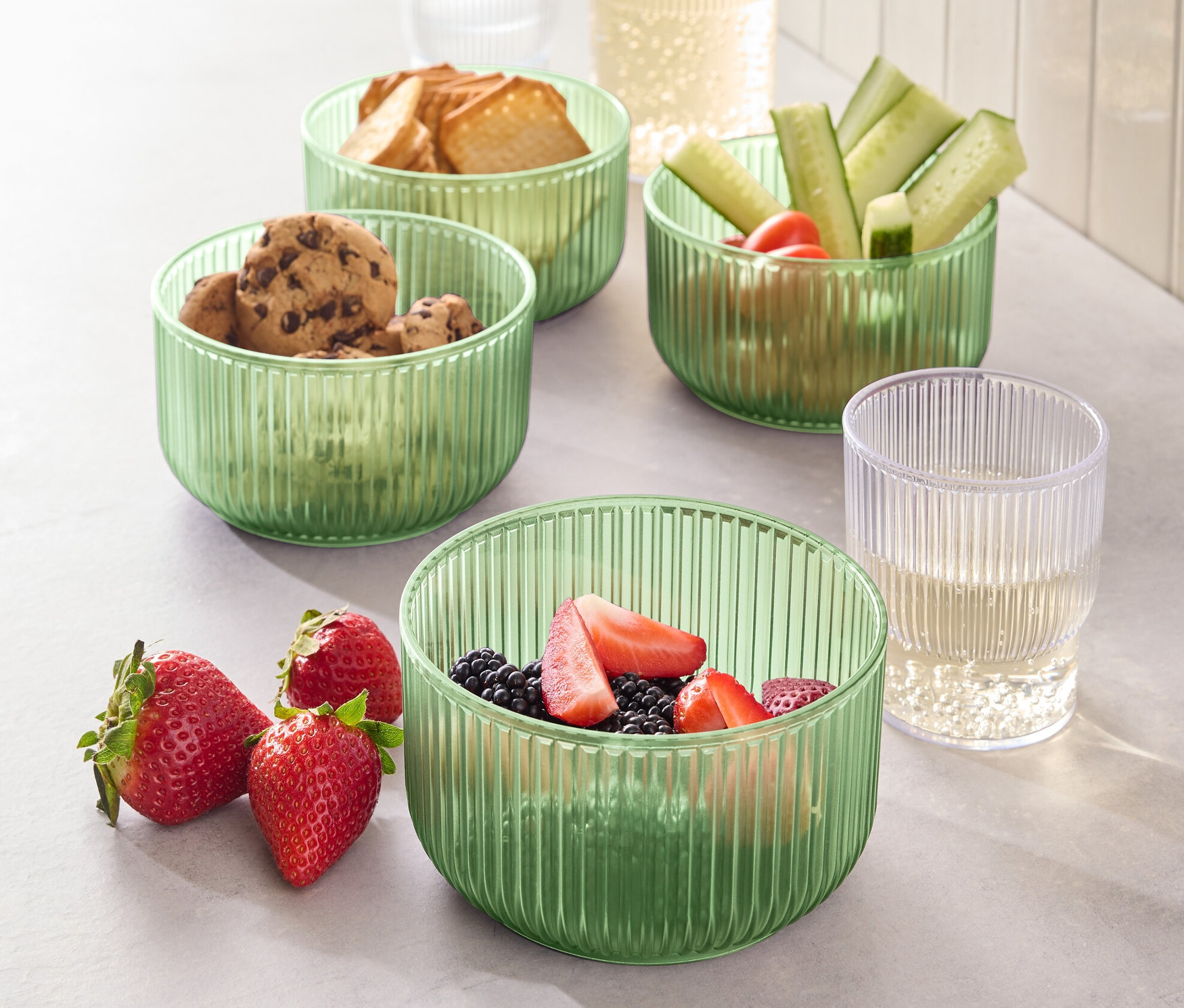 Čtyři plastové misky s jídlem, včetně sušenek, chleba, okurek a jahod.