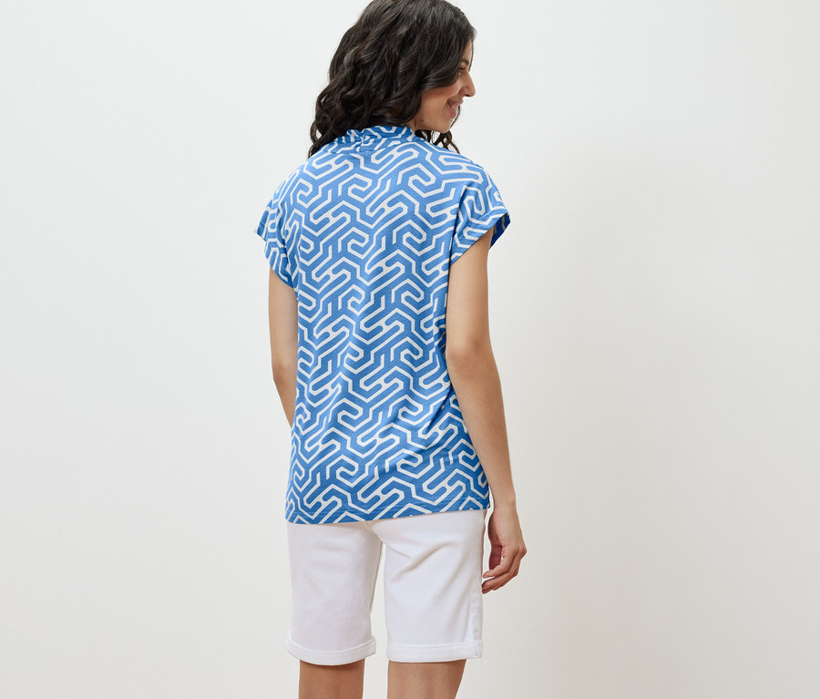 Žena má na sobě modré halenkové triko s výstřihem do V a bílé šortky.