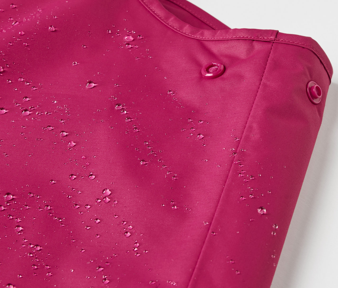 Detail dětských termo kalhot do deště bobulové barvy s kapkami vody.