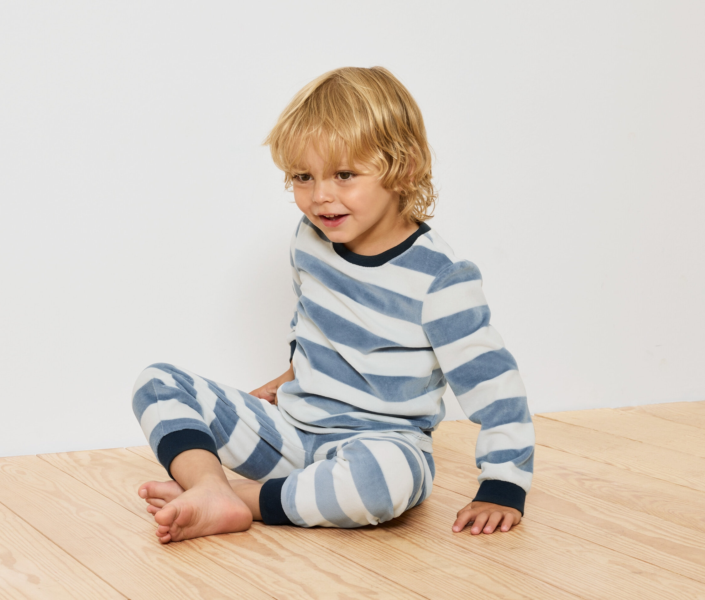 Chlapec sedí na dřevěné podlaze v pruhovaném pyžamu.