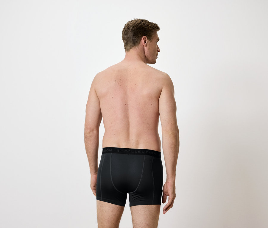 Záda muže v černých boxerkách na bílém pozadí.