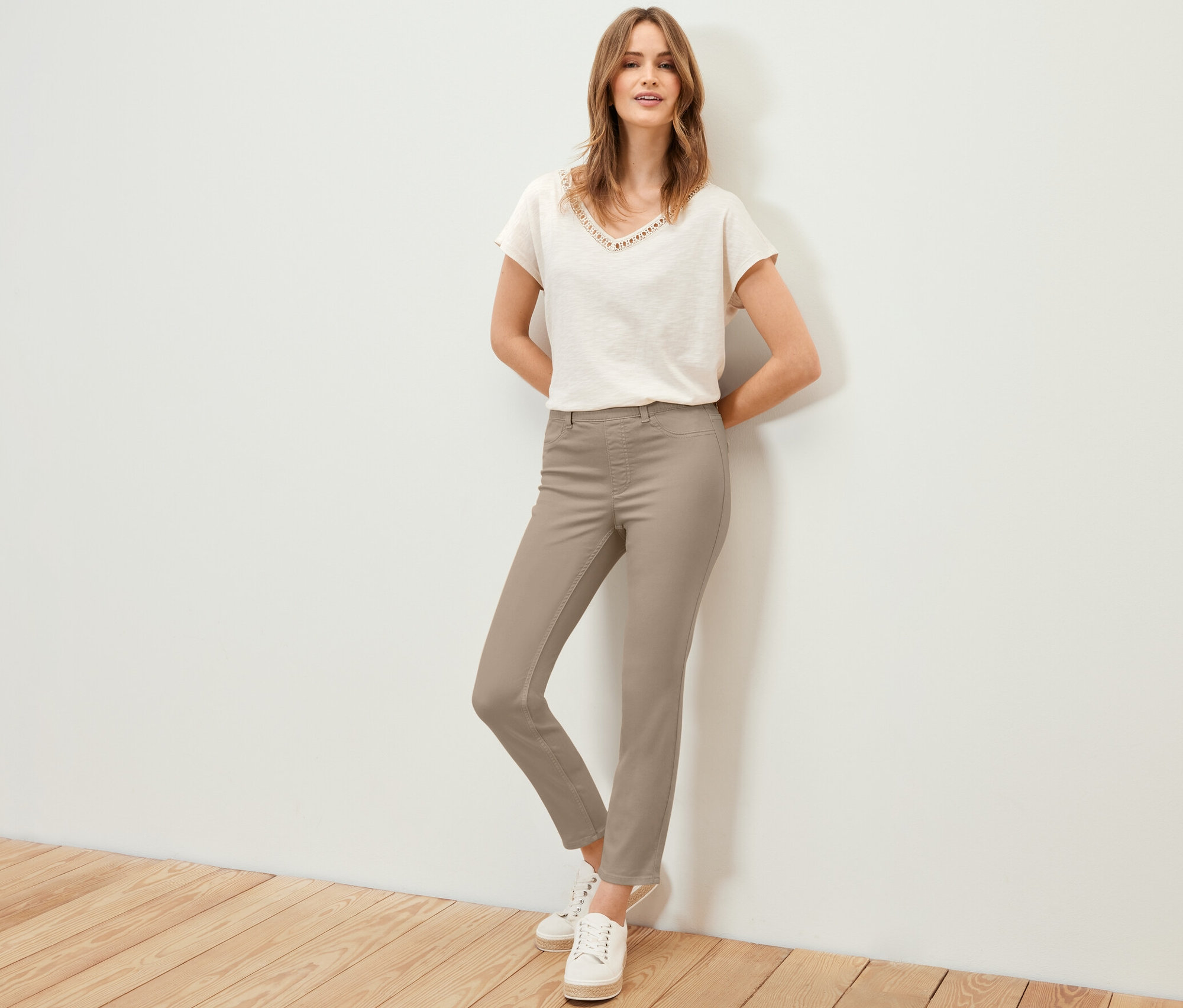 Žena pózuje v 7/8 tregínech, tričku a teniskách.