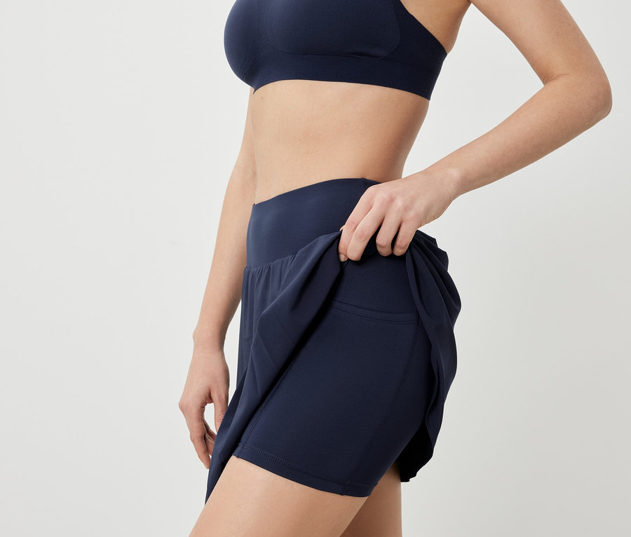 Žena pózuje ve sportovní podprsence a tmavě modré sportovní sukni.