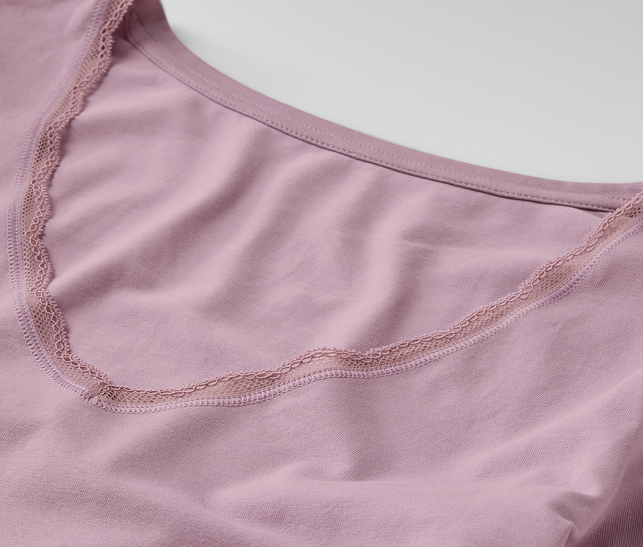 Detail fialového tílka s dlouhým rukávem a krajkovým lemem.