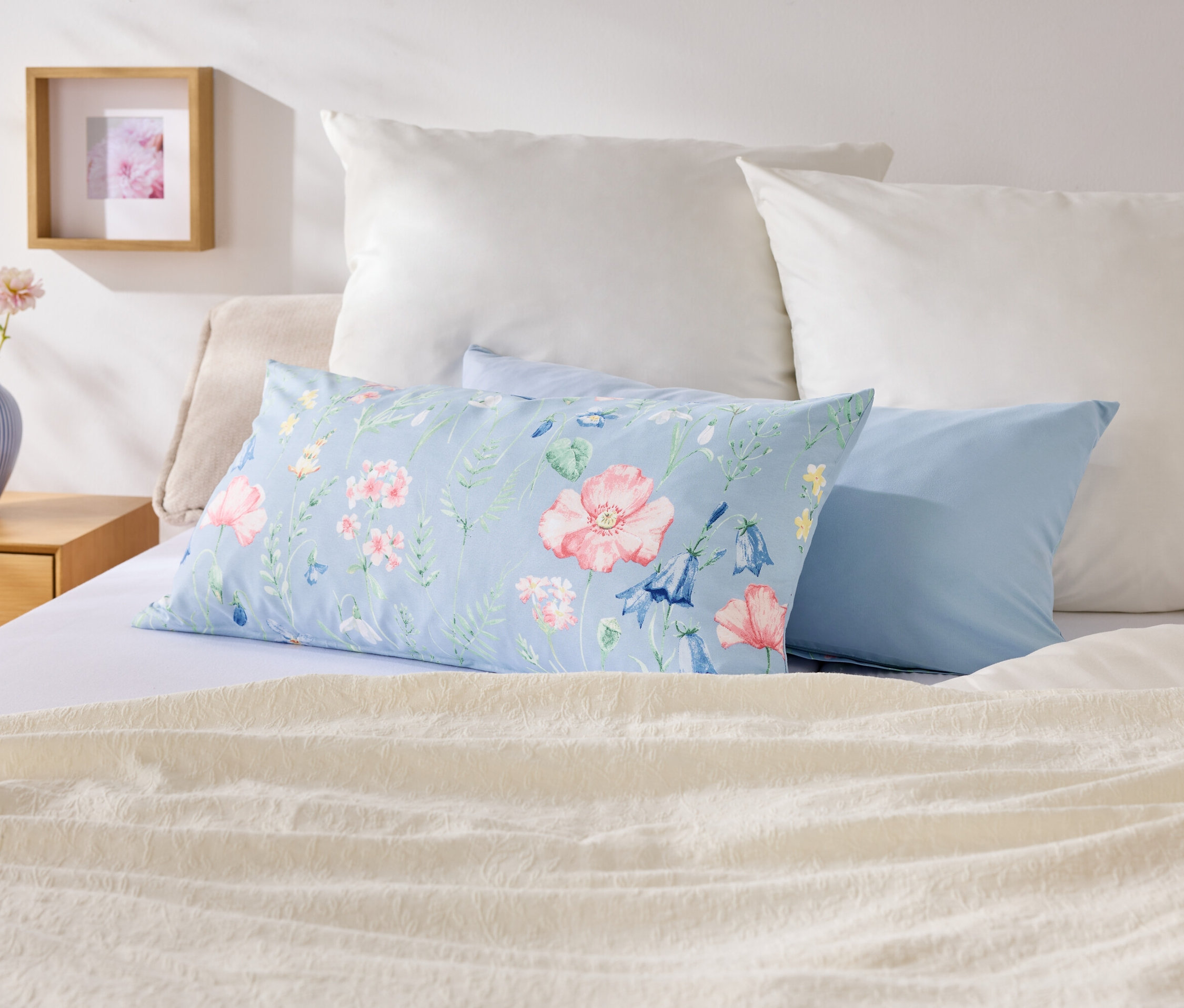 Na posteli leží polštáře různých barev a vzorů.