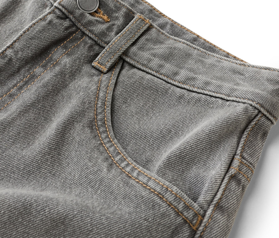 Detailní záběr šedých džínů s kapsou a knoflíkem.