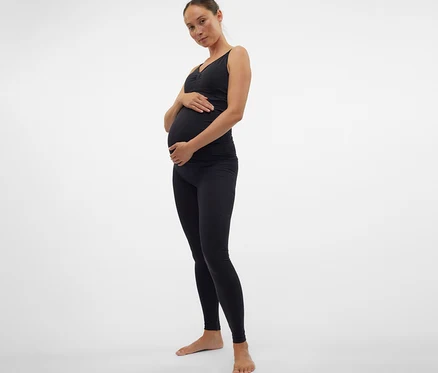 Těhotná žena v černém topu a skinny legínách MAMALICIOUS »MLTIA JEANNE« si drží břicho.