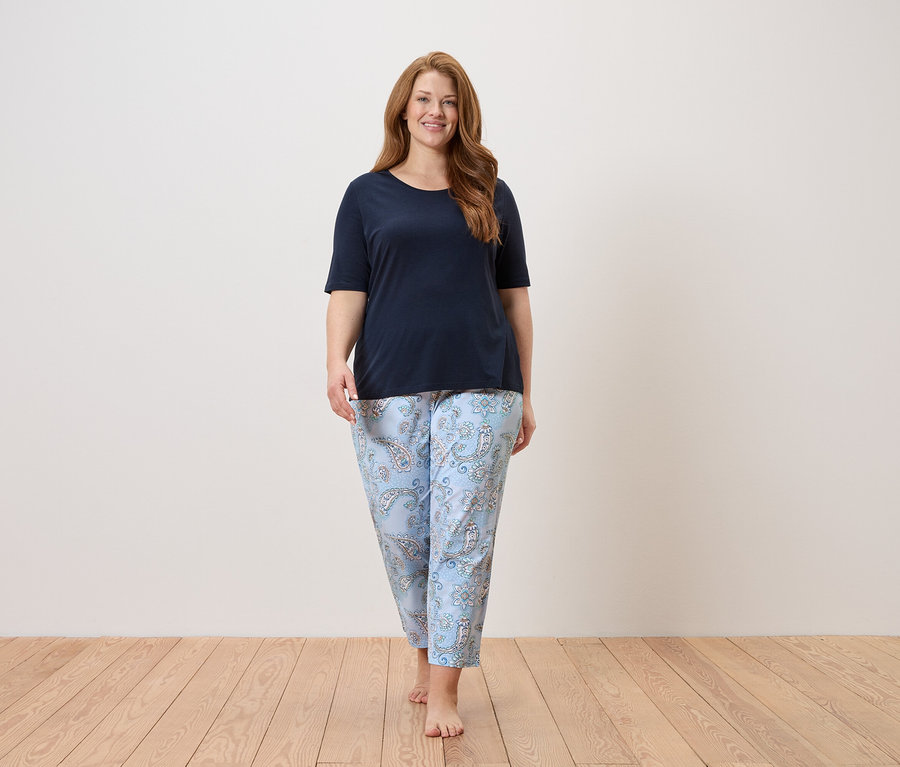 Žena kráčí bosá v tmavě modrém topu a světle modrých kalhotách s paisley vzorem.
