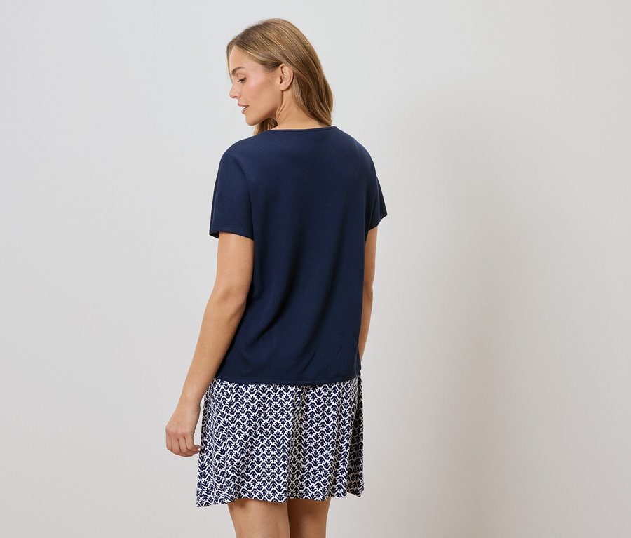 Pohled zezadu na ženu s blond vlasy v tmavě modrém tričku a sukni s modrobílým vzorem.
