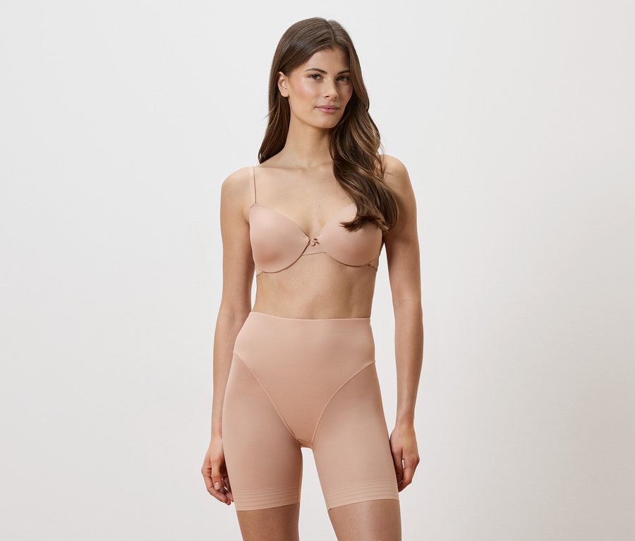 Žena má na sobě tělovou podprsenku a tvarovací šortky na bílém pozadí.